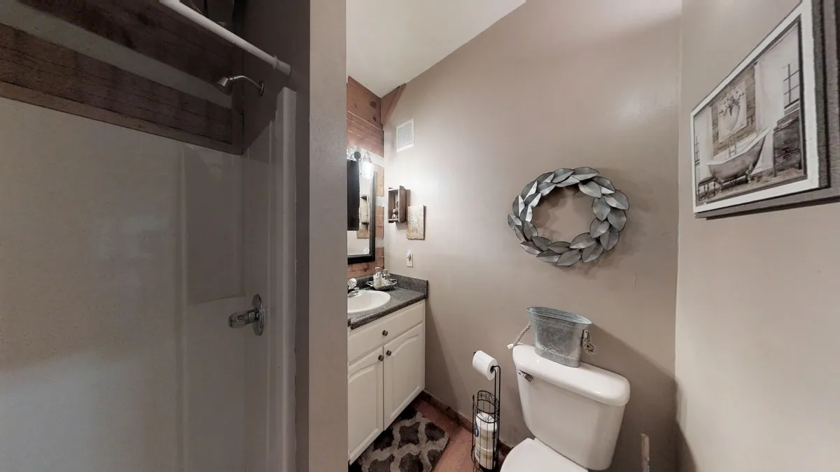 A serene bathroom featuring a modern vanity with mirror, a walk-in shower area, and tasteful accent decor such as a decorative wreath and coordinated accessories. The layout suggests comfort and practical use, ideal for daily routines and relaxation.