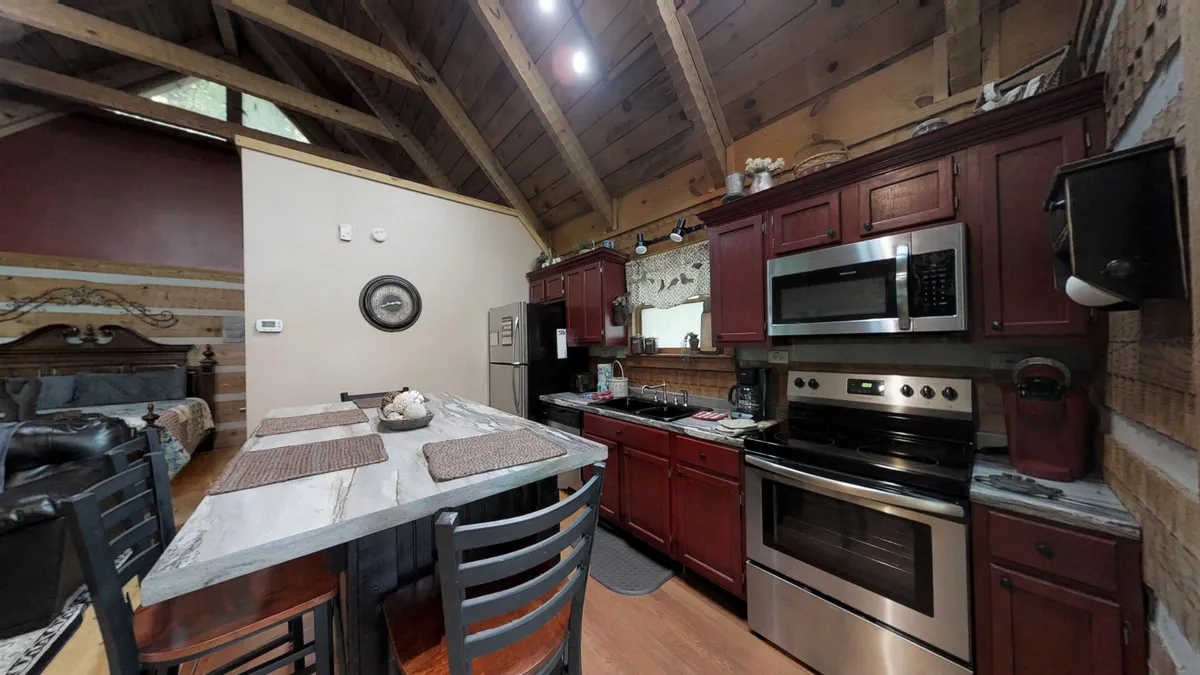 A cozy kitchen scene featuring a prominent kitchen island with seating, vibrant red cabinetry, exposed wooden beams, and essential appliances. The setting invites group interaction and culinary creativity, evoking a sense of warmth and togetherness.