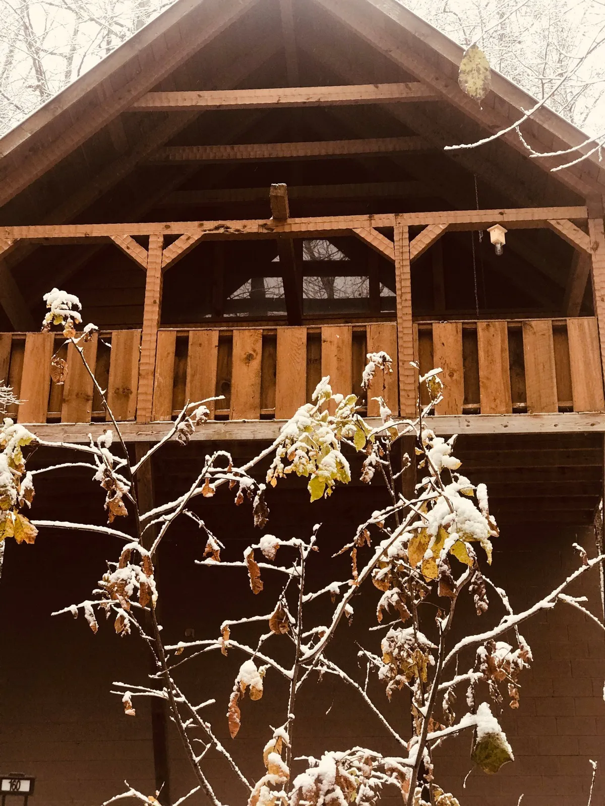 A wooden balcony with snow-dusted branches and classic log cabin architecture, inviting guests to step outside and enjoy the fresh mountain air. The setting is tranquil and intimate, ideal for sunset strolls and hot tub relaxation.