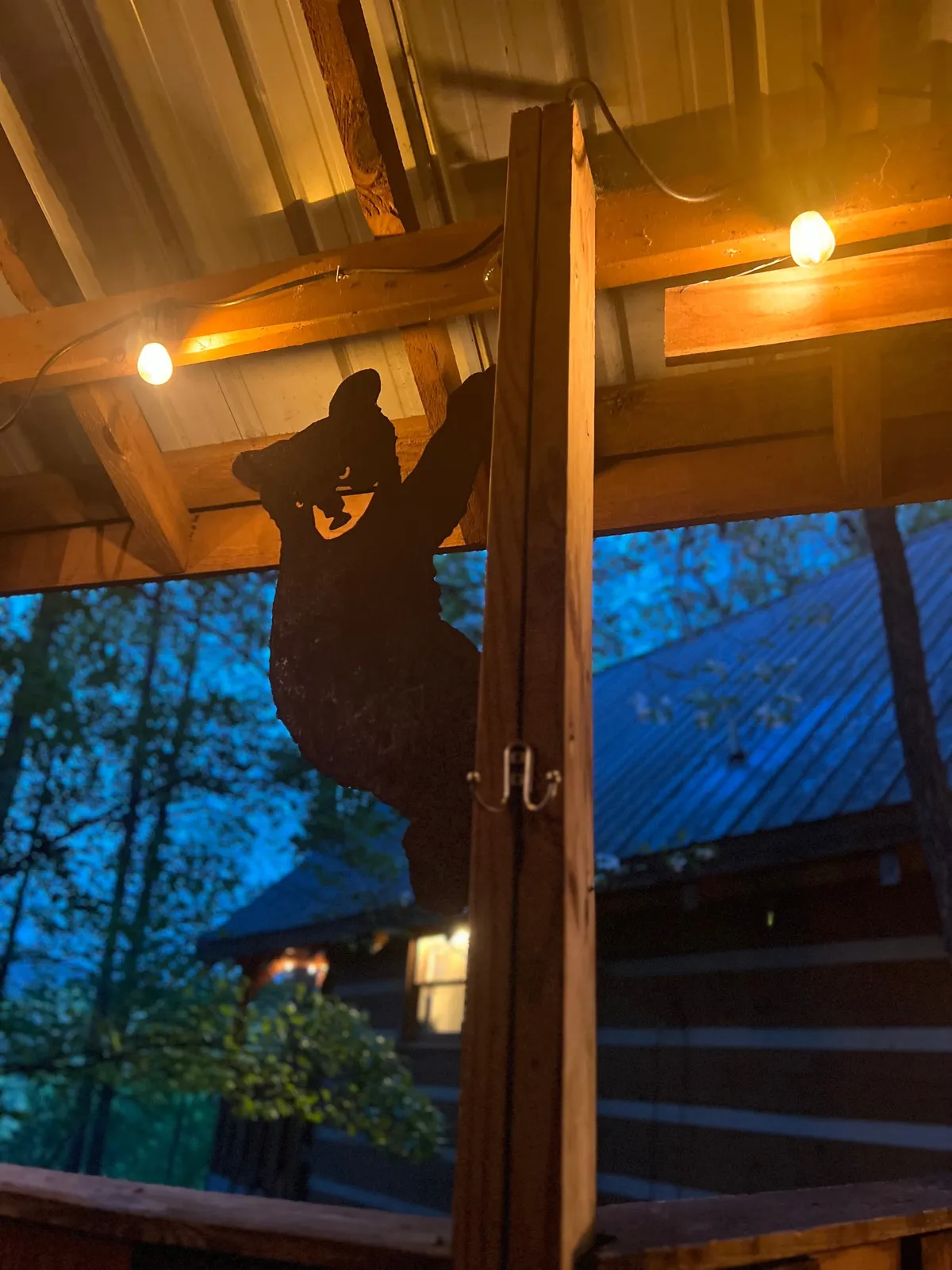 A playful exterior setting featuring a bear silhouette, string lights, and a wooden structure. The space invites groups to gather for nighttime storytelling, games, or simply enjoying the outdoors under the stars.