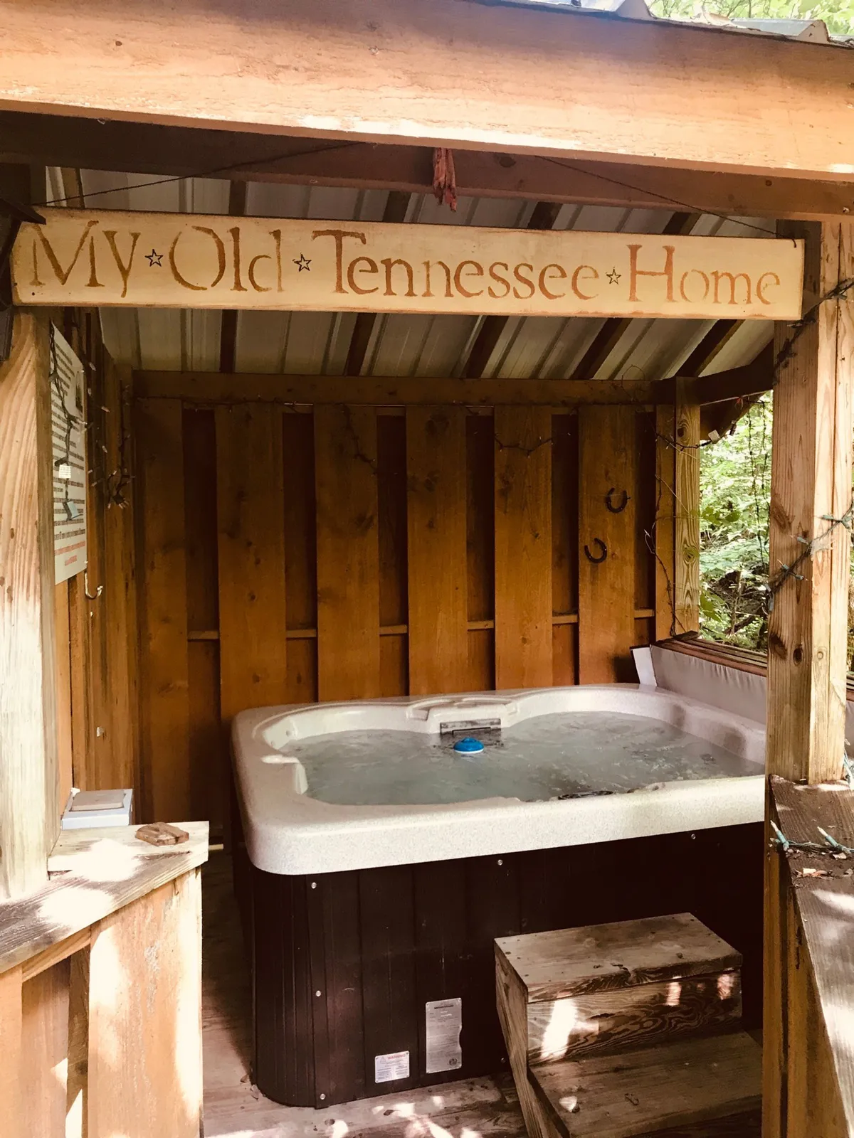 This image features a hot tub set on a private deck, accented by rustic wood finishes and a welcoming wooden sign. The space is clearly designed for both relaxation and social gatherings, with inviting views of the surrounding nature visible beyond the deck railing.