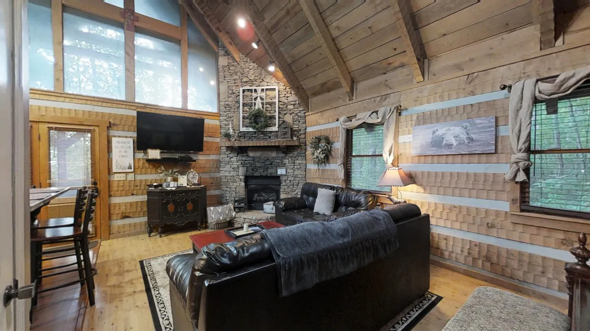 A warm, open-concept living area featuring a rustic stone fireplace as the centerpiece. Large windows bring in daylight, wooden beams add architectural character, and plush seating invites relaxation. This space seamlessly blends lounging and socializing, reflecting the studio's heart.