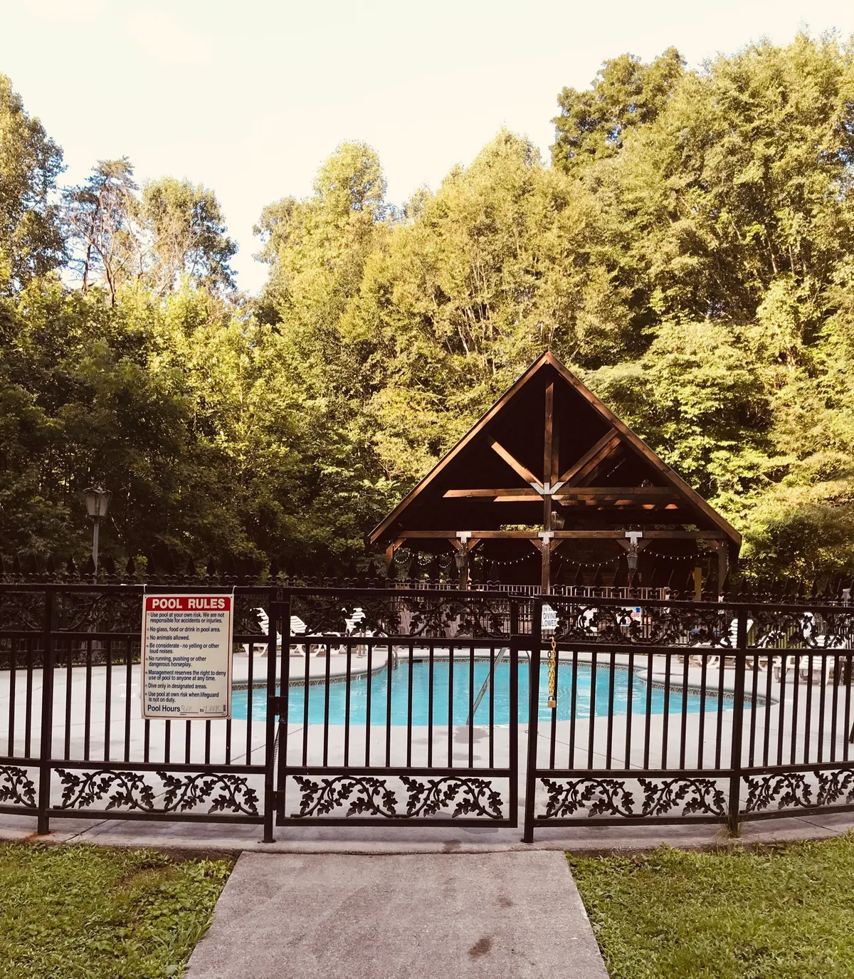 A resort-style swimming pool sits beside a charming gazebo, enclosed by a decorative fence. The area is designed for swimming, sunbathing, and community gatherings, evoking relaxation and family fun.