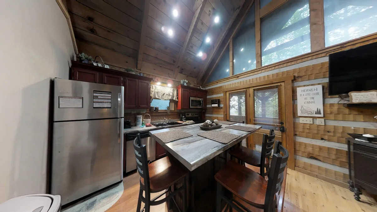 A welcoming kitchen featuring a spacious island with seating, modern stainless steel appliances, wooden ceiling beams, and large windows that let in natural light. The layout highlights the kitchen as a central gathering space, with the island perfect for casual dining, conversation, and meal prep.