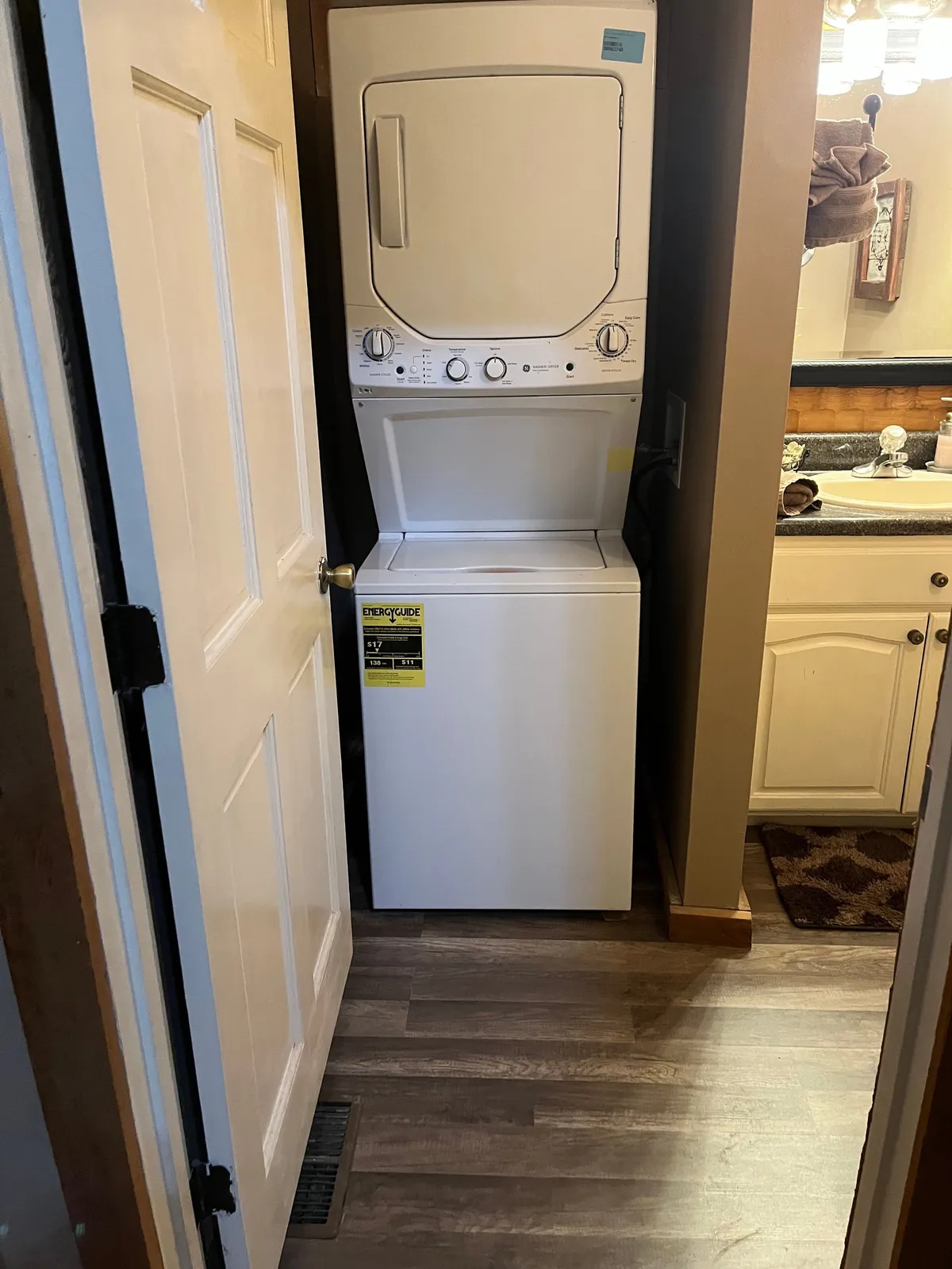 A practical, efficient bathroom space equipped with a stackable washer and dryer, a bathroom vanity with a mirror, and an accessible towel rack. The space is tidy, well-lit, and designed for convenience.